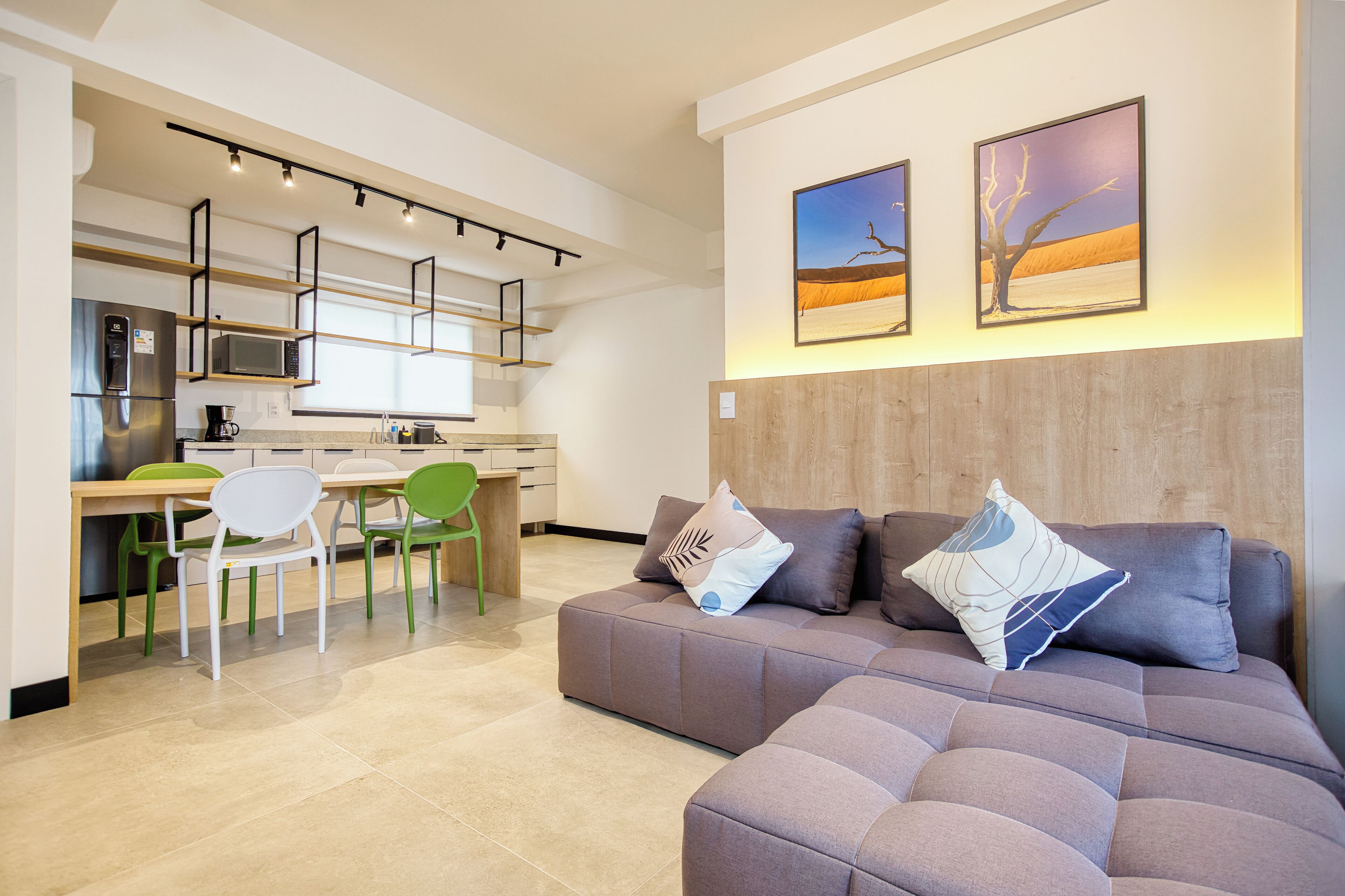 A modern living room with a sectional sofa, a dining area with a table and chairs, and a kitchen with a microwave and refrigerator.