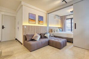 Ein modernes Hotelzimmer mit Ecksofa, einem Bett und einem großen Fenster.