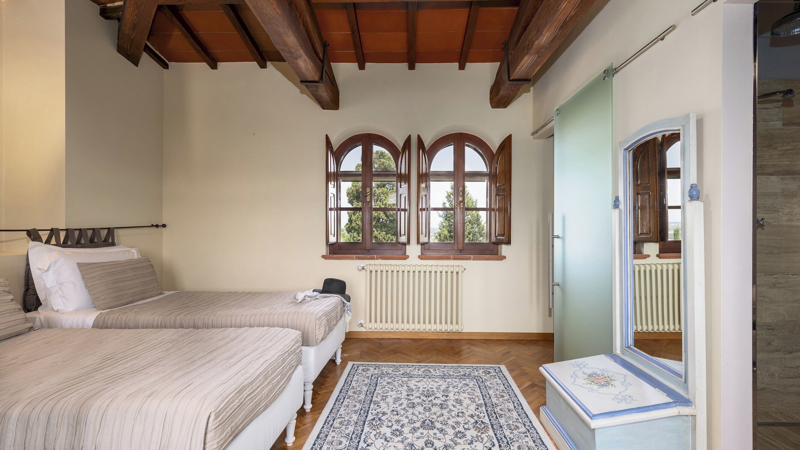Ein Schlafzimmer mit zwei Betten, einem Heizkörper, einem Fenster mit Holzläden und einem Spiegel.