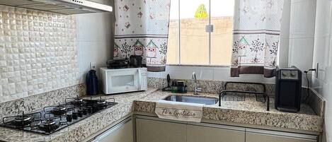 A kitchen with a gas stove, microwave, sink, and a window with curtains.