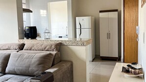 Un espacio habitable compacto con sofá, una pequeña zona de cocina que incluye un refrigerador y un microondas, y una puerta de madera.