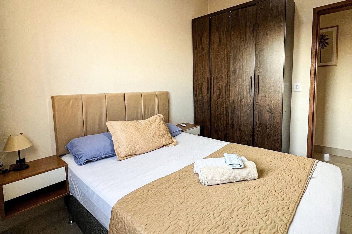 A hotel room with a bed, a nightstand, a wardrobe, and a framed picture on the wall.