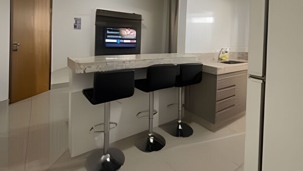 Una cocina moderna con una isla integrada, tres taburetes negros y un refrigerador. Encima de la isla, hay un televisor montado.