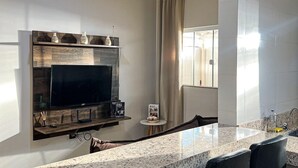 Una cocina moderna con encimera de granito, taburetes de bar negros, televisor de pantalla plana y una mesita auxiliar con una revista.