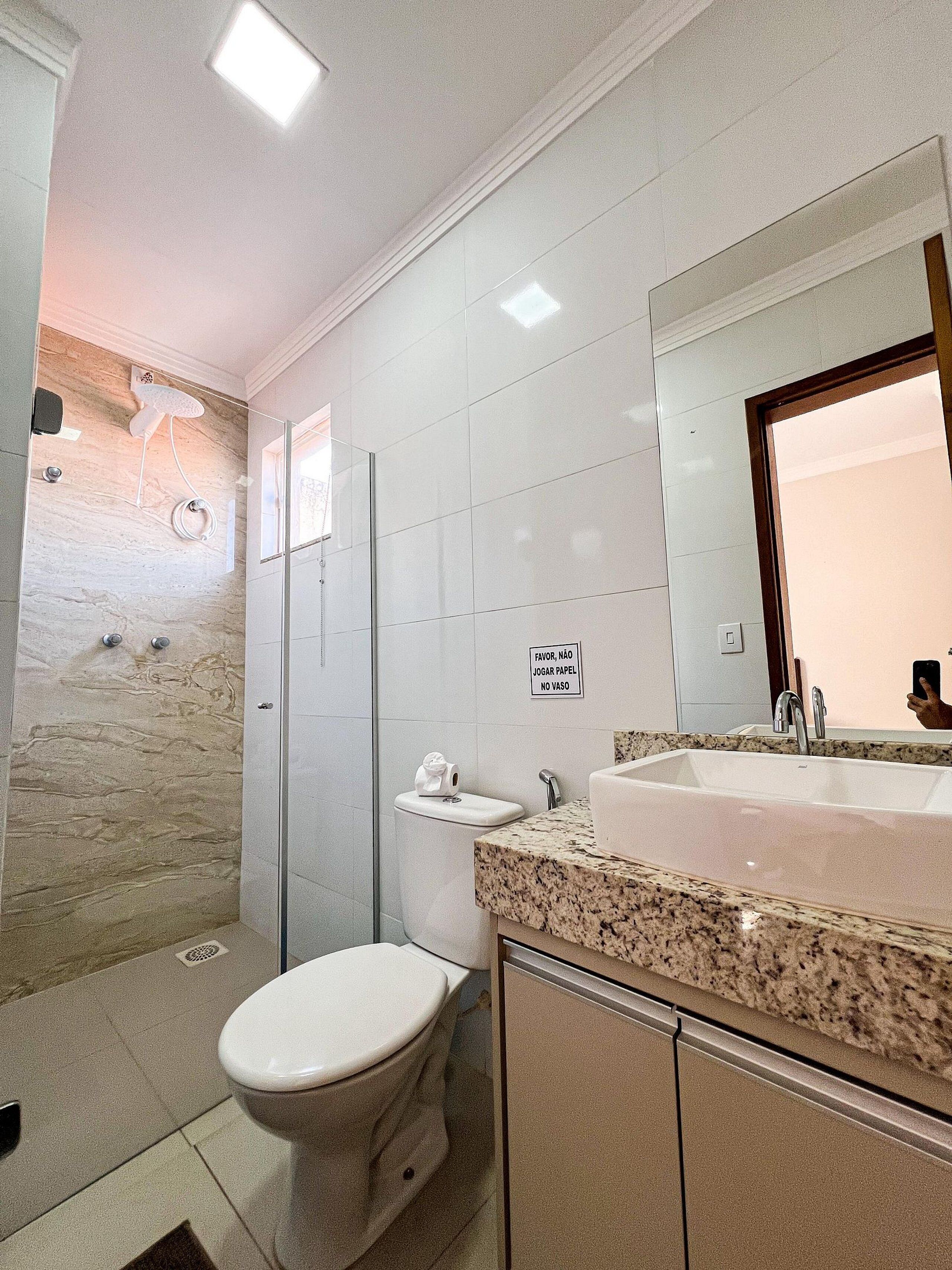 A modern bathroom with a marble shower, a toilet, and a sink with a granite countertop.