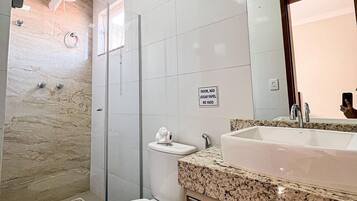 A modern bathroom with a marble shower, a toilet, and a sink with a granite countertop.