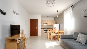 Een moderne woonkamer met een grijze bank, een houten tv-meubel en een eethoek met een tafel en stoelen.