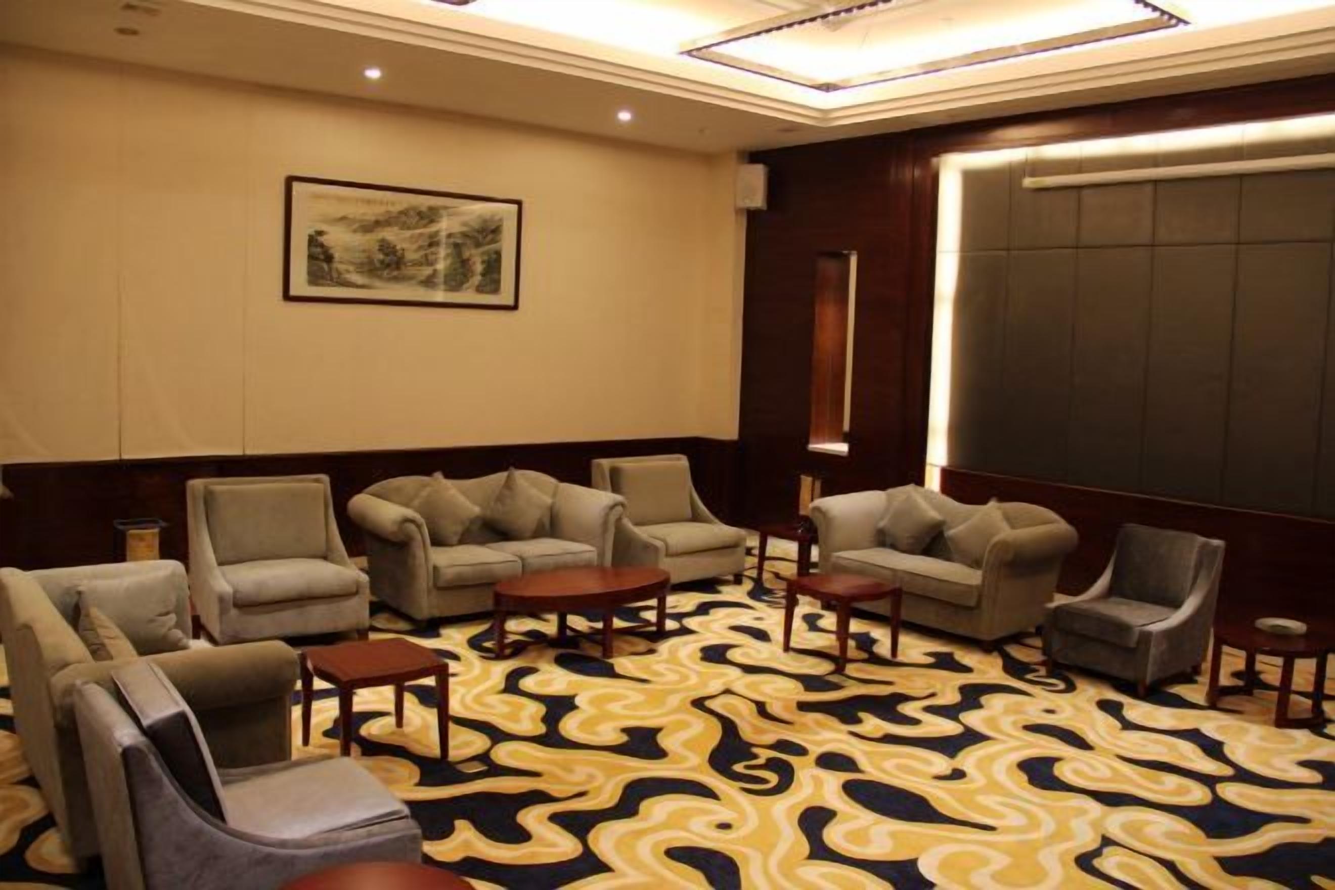 A hotel room with a patterned carpet, multiple seating options including sofas and chairs, a small table, and a large window.