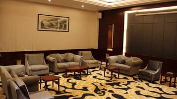 A hotel room with a patterned carpet, multiple seating options including sofas and chairs, a small table, and a large window.