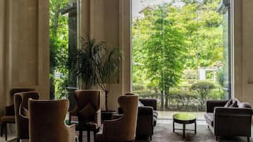A lobby with multiple seating areas, a large window with a view of greenery, and a potted plant.