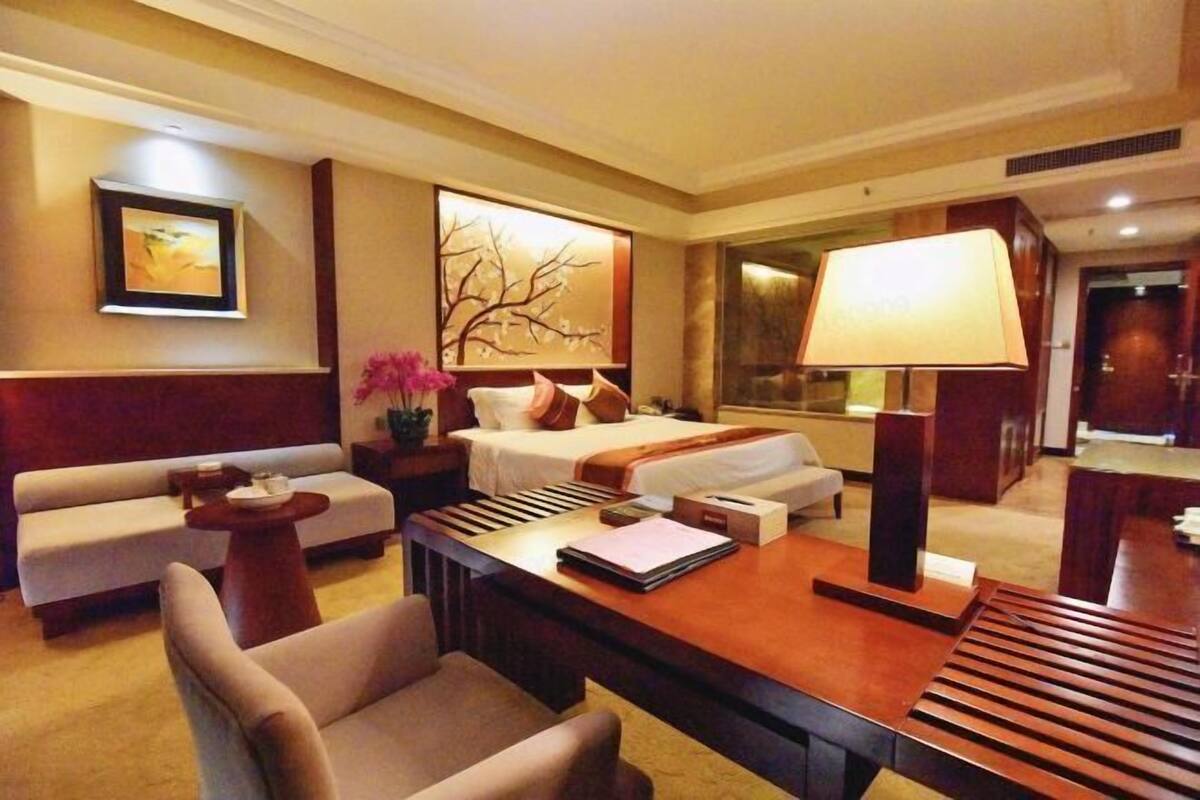 Une chambre d’hôtel avec un canapé, un lit, un bureau, une lampe et un tableau au mur.
