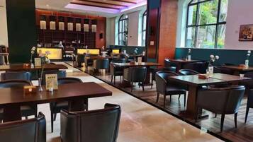 A spacious restaurant with multiple tables and chairs, a bar area, and large windows providing natural light.