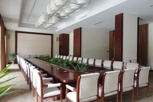 Un salón de conferencias con una larga mesa y sillas, un candelabro y una planta en maceta.