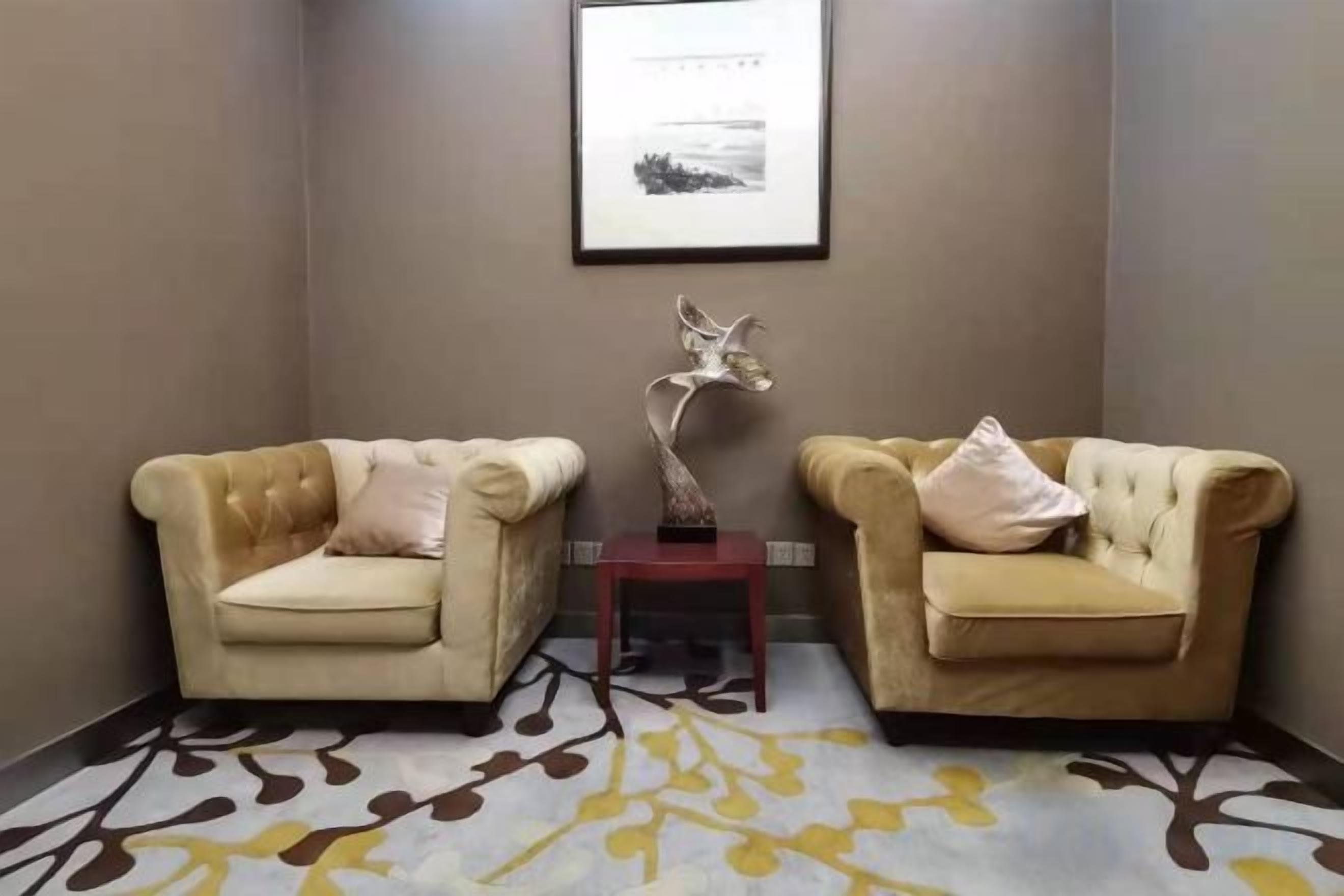 A corner room with two armchairs, a small table, and a framed picture on the wall.