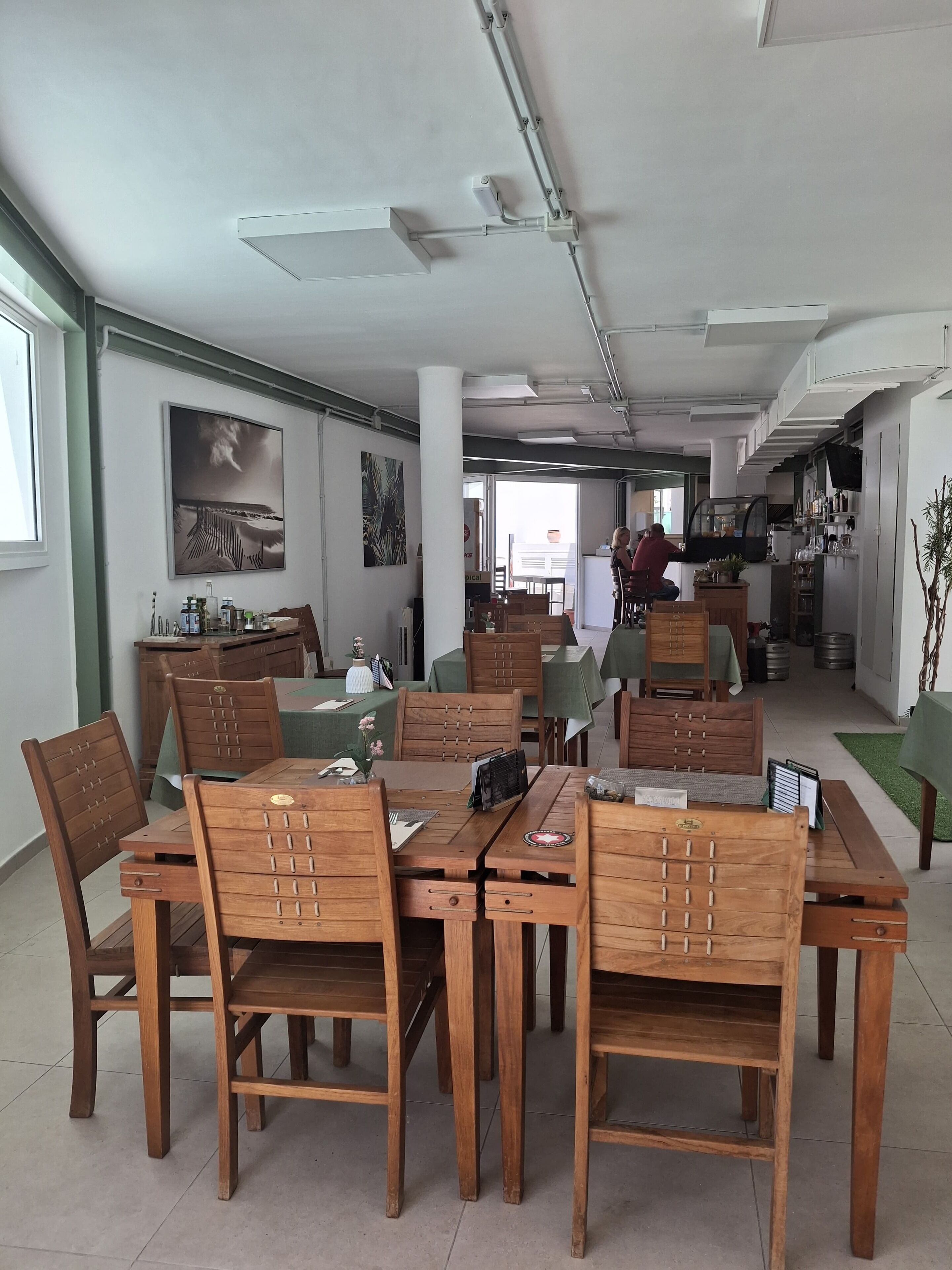 Un comedor amplio con mesas y sillas de madera, un cuadro grande en la pared y vistas al área de la cocina.