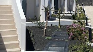 A modern white building with multiple entry points, a staircase, and a landscaped garden with cacti and flowers. - Kikerestudios (Puerto del Carmen)