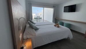A hotel room with two beds, a TV on the wall, and a balcony with a table and chairs. - Kikerestudios (Puerto del Carmen)