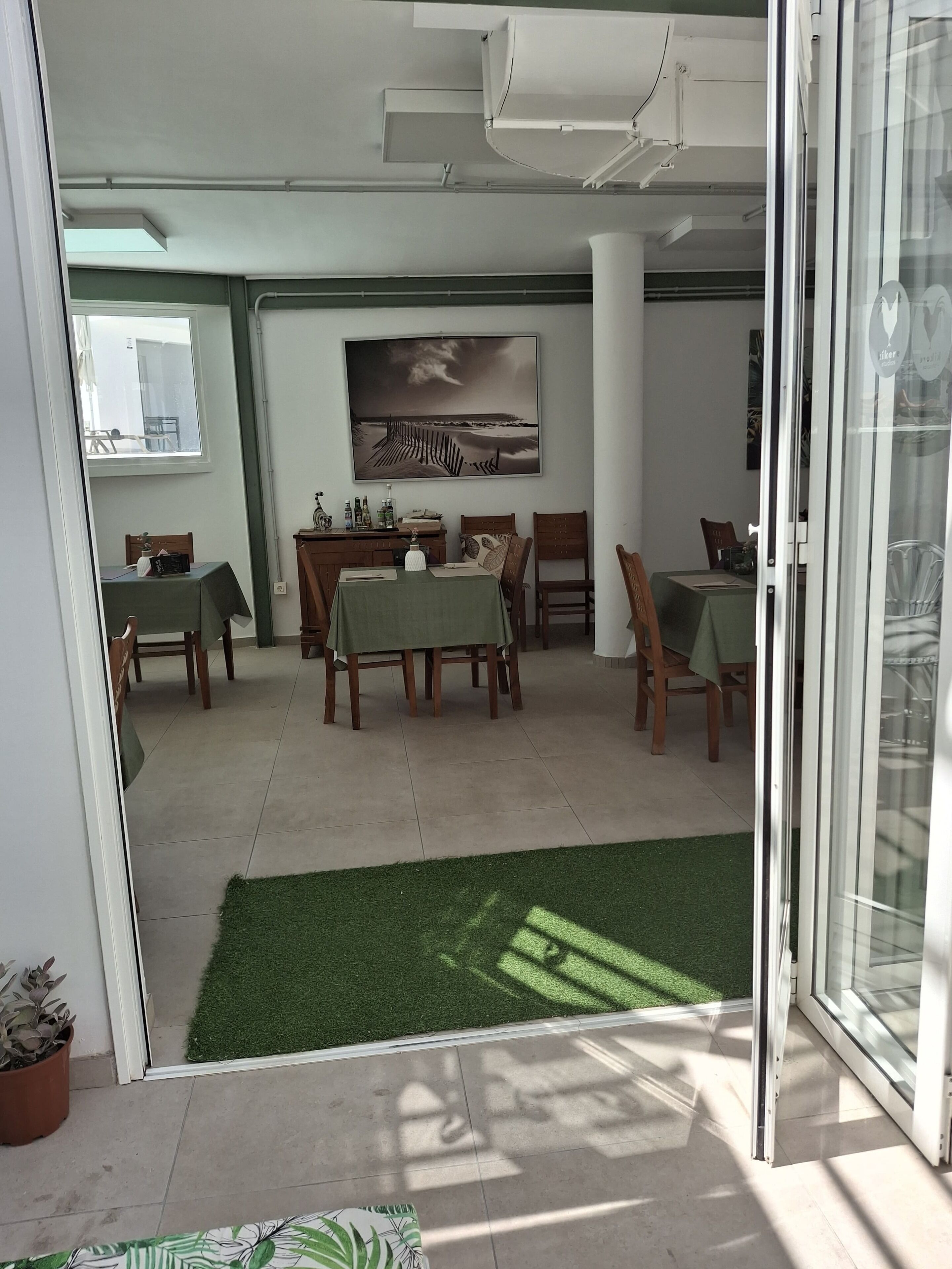 Un área de comedor con mesas y sillas, un cuadro en la pared y vistas a través de un ventanal.
