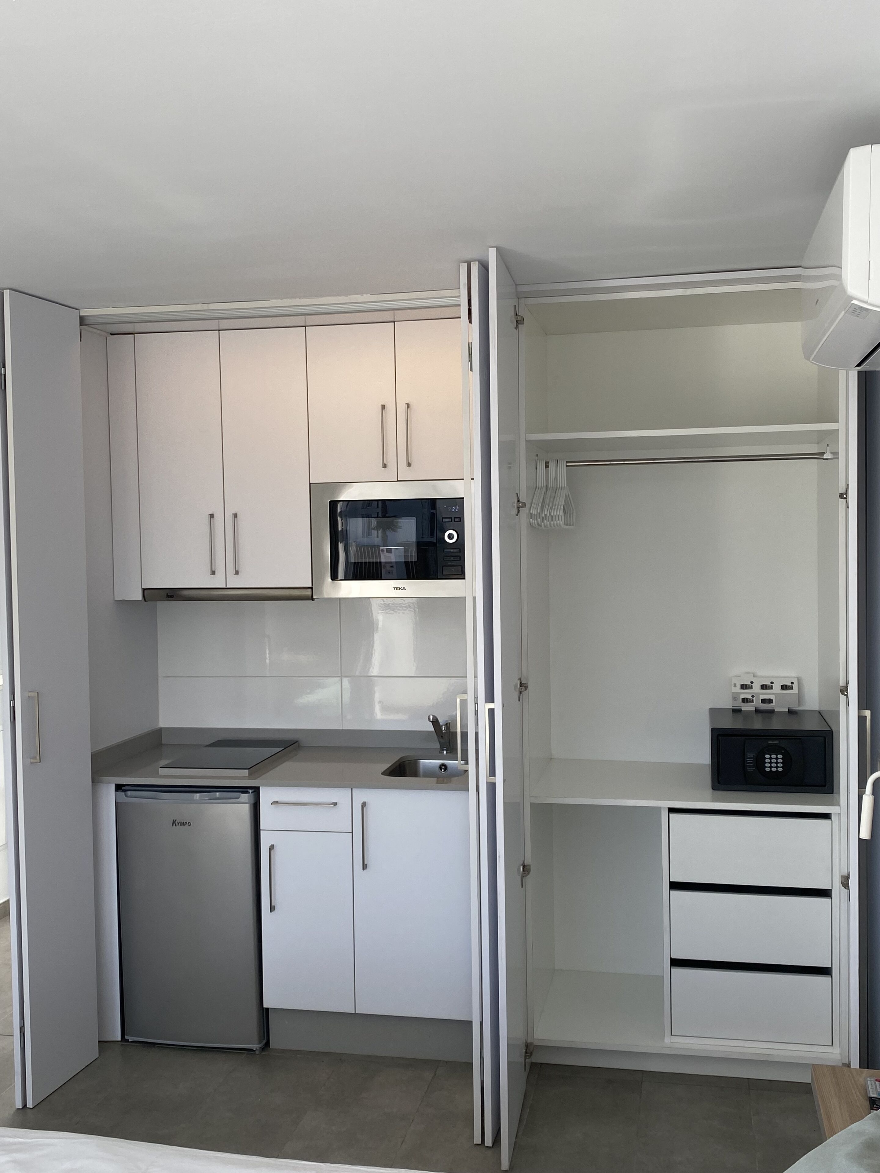 Una cocina compacta con armarios blancos, microondas integrado, lavavajillas y un refrigerador pequeño.