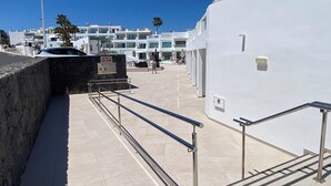 A modern building with a white facade, a stone wall, and a tiled floor. - Kikerestudios (Puerto del Carmen)