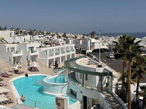 A modern hotel with a pool area, multiple balconies, and a view of the surrounding town and ocean. - Kikerestudios (Puerto del Carmen)