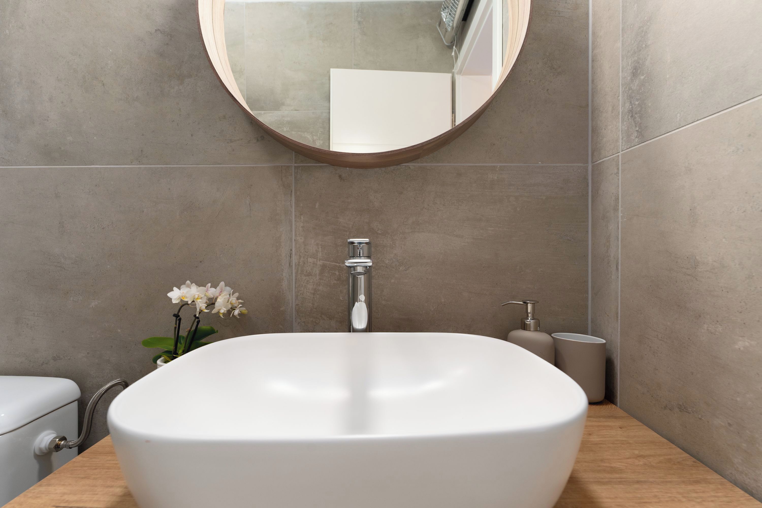 Une salle de bain avec un lavabo blanc, un miroir rond et des toilettes.