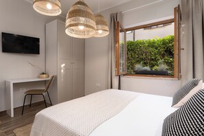 Ein Schlafzimmer mit Bett, Schreibtisch, Stuhl, Fernseher und einem Fenster mit Blick auf Grünflächen.
