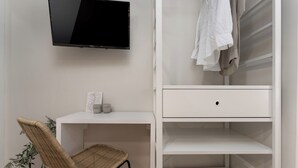 A white desk with a chair, a television mounted on the wall, and a white wardrobe with hanging clothes. - Studio apartment Alloro One (Istria - Novigrad) (Novigrad)
