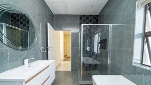 A modern bathroom with a white vanity, a glass shower enclosure, and a large mirror. - Ada 5 (Bedfordview)