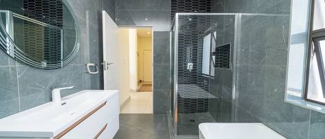 A modern bathroom with a white vanity, a glass shower enclosure, and a large mirror.