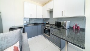 A modern kitchen with grey cabinets, a black countertop, and stainless steel appliances. - Ada 5 (Bedfordview)