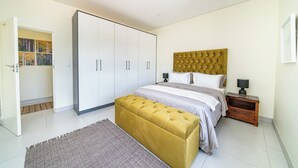 A bedroom with a bed, a large wardrobe, a bedside table, and a floor lamp. - Ada 5 (Bedfordview)