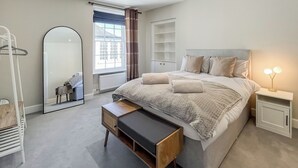 A bedroom with a bed, bedside tables, a mirror, a bench, and a window with curtains. - Murray Street Town House (Duns)