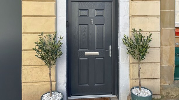 A dark grey door with the name "MURRAYST" above it, flanked by two small potted plants. - Murray Street Town House (Duns)