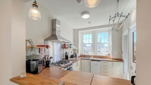 A modern kitchen with a wooden countertop, stainless steel appliances, and a large window providing natural light. - Murray Street Town House (Duns)