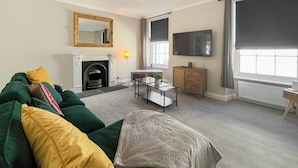 A living room with a green sofa, a fireplace, a television, and a window with curtains. - Murray Street Town House (Duns)