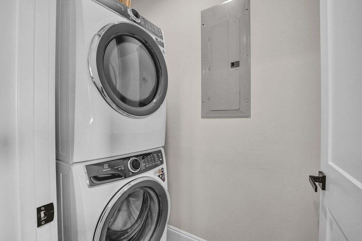 A laundry area with stacked washers and dryers, a utility door, and a wall-mounted electrical panel.