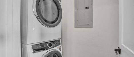 A laundry area with stacked washers and dryers, a utility door, and a wall-mounted electrical panel.