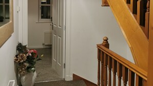 Un pasillo con una escalera de madera, una puerta blanca y una planta en maceta.