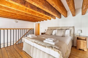 Ein Schlafzimmer mit einem großen Bett, Holzbalken, einer Treppe und einem Nachttisch.