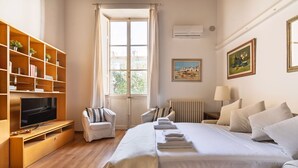 Ein Hotelzimmer mit Bett, Fernseher, Bücherregal und einem Fenster mit Vorhängen.