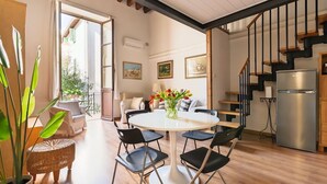 Ein geräumiges Wohnzimmer mit einem runden Tisch, schwarzen Stühlen, einem Korbsessel und einem Blumentopf, mit Blick ins Freie.