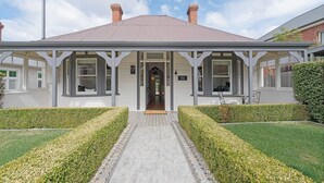 A two-story house with a front porch, a central door, and a small garden with hedges.
