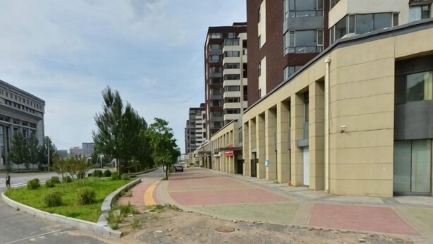 A building with a flat facade, a paved walkway, and a landscaped area with grass and trees. - Huanren Qingfeng Hotel (Huanren)