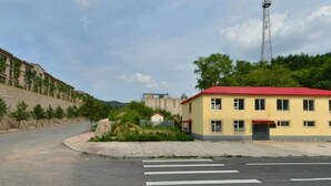 A building with a red roof, a paved road with a pedestrian crossing, and a clear sky. - Huanren Qingfeng Hotel (Huanren)