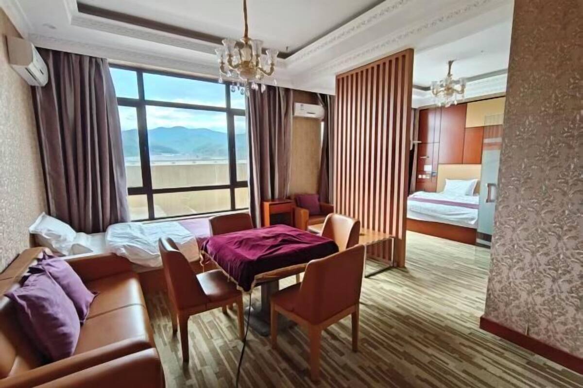 Quarto de hotel com uma cama, uma mesa com cadeira, um sofá, uma janela com cortinas e vista para as montanhas.