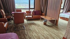 A hotel room with a sofa, chairs, a small table, a bed, and large windows with a view. - Huanren Qingfeng Hotel (Huanren)