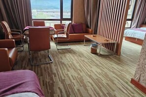 A hotel room with a sofa, chairs, a small table, a bed, and large windows with a view. - Huanren Qingfeng Hotel (Huanren)