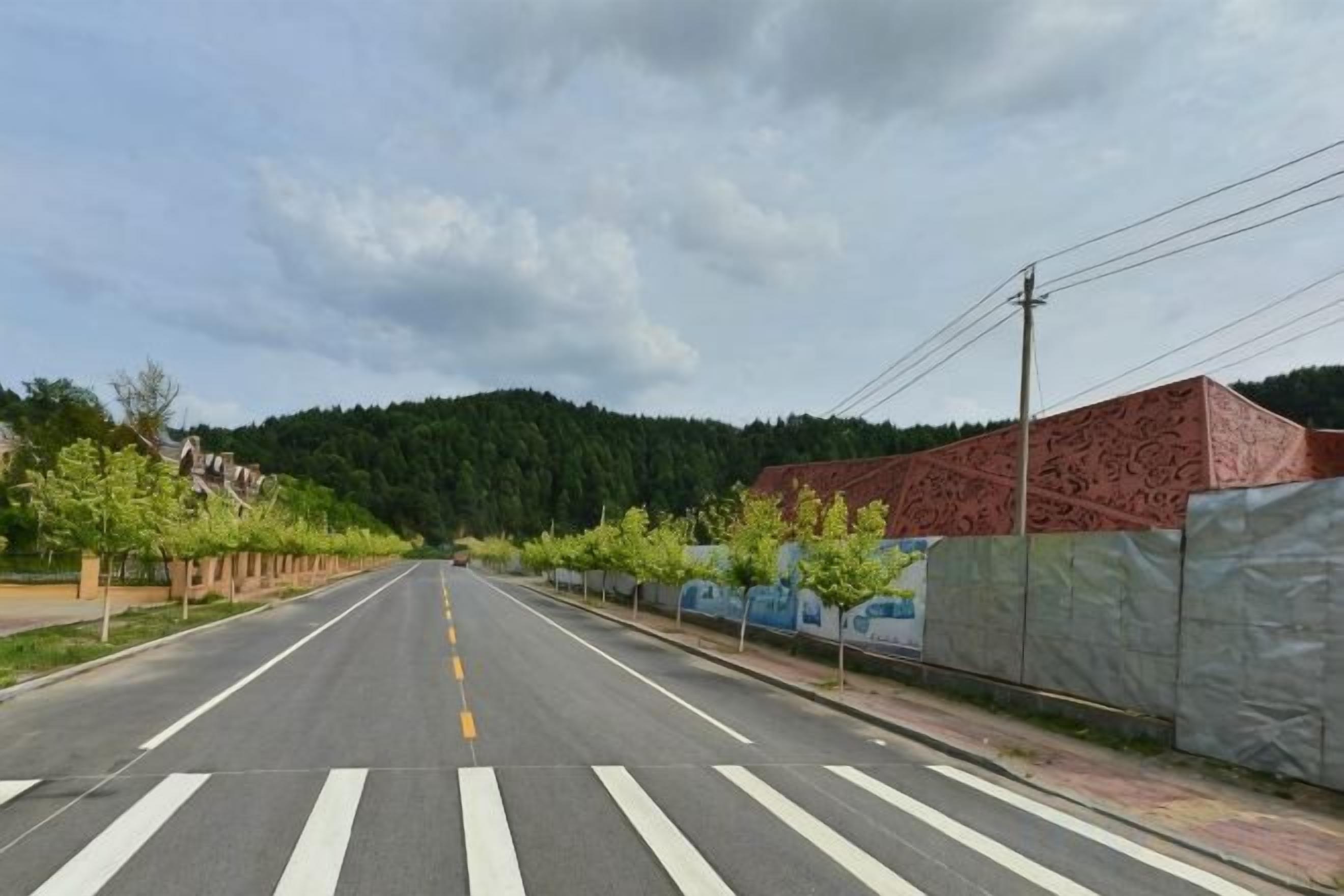Eine gerade Straße mit einer Fußgängerüberweg, gesäumt von Bäumen und einem Gebäude mit roter Fassade.