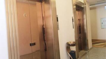 An elevator with a metallic finish, a visible emergency phone, and a wall-mounted light switch.